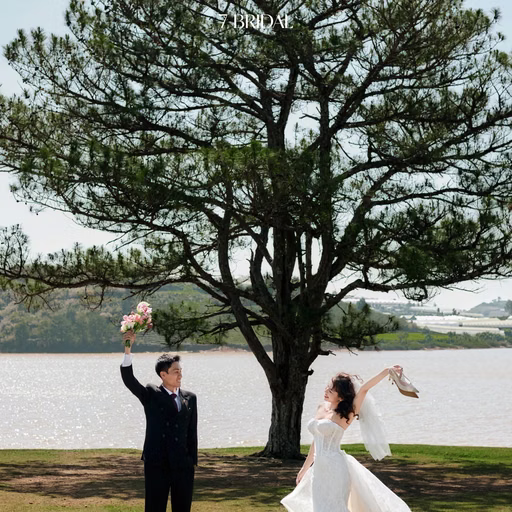 The couple raise their hands and bouquet before the lakeside pine at Cây Thông Cô Đơn, Đà Lạt