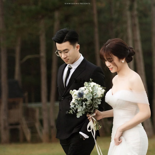 The bride and groom walk together with a white bouquet beside the pine forest.