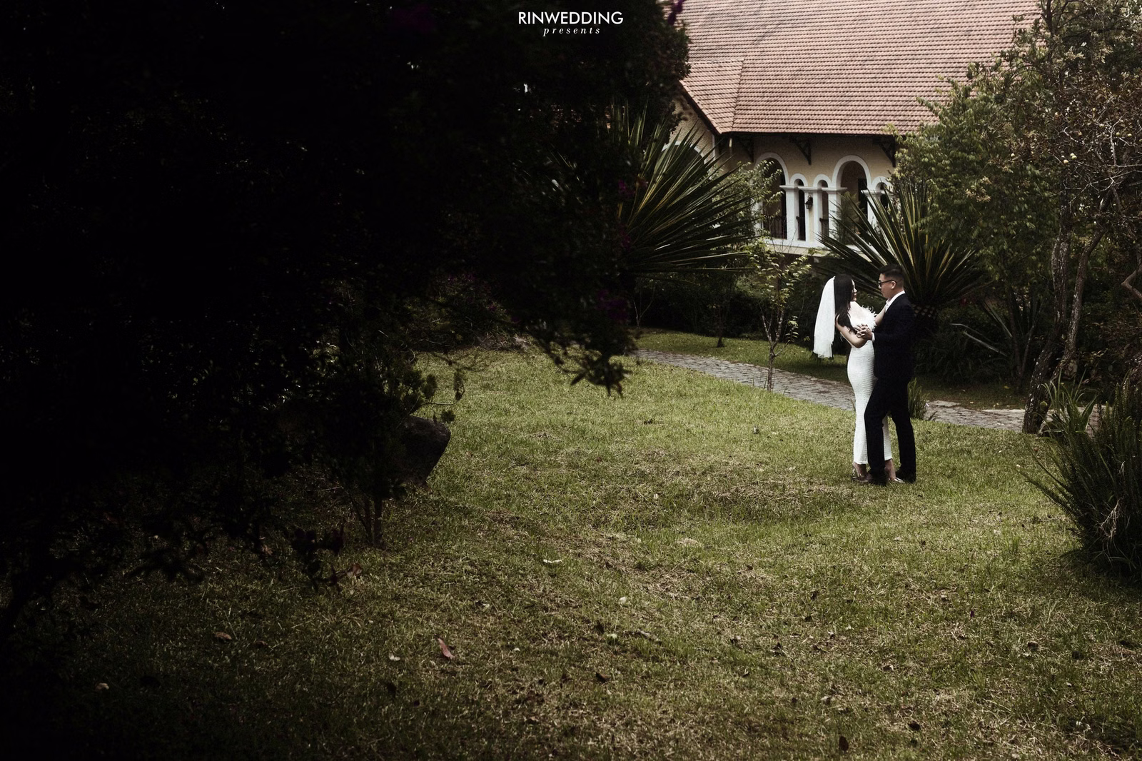 A bride and groom embrace on the lawn before a villa.