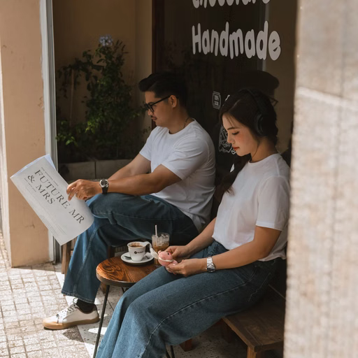 The couple in white sit reading a newspaper and drinking coffee outside a Đà Lạt shop.