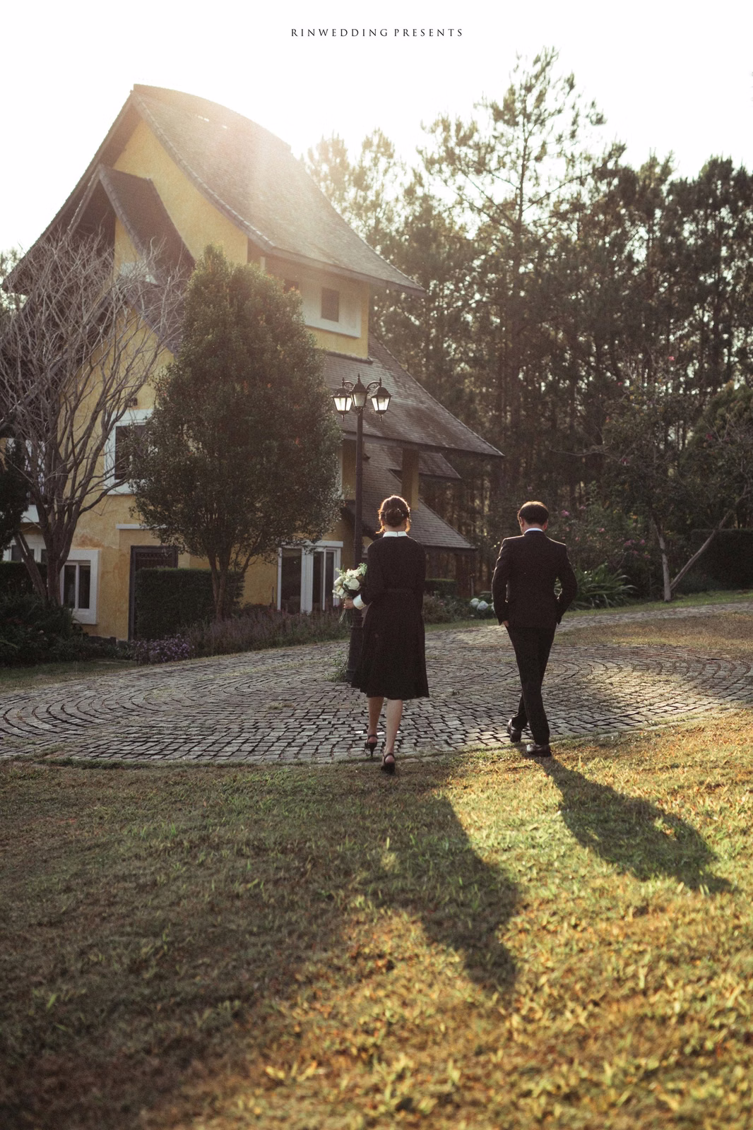 The bride and groom walking hand in hand before a sunlit villa.