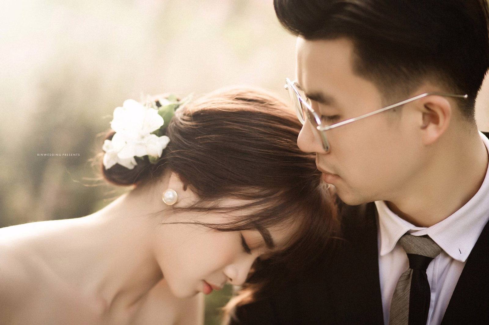 The groom kissing the bride’s hair in soft sunlight in the resort garden.