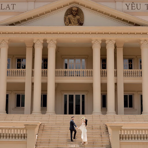 The bride and groom stand on the steps at Nhà thờ Don Bosco