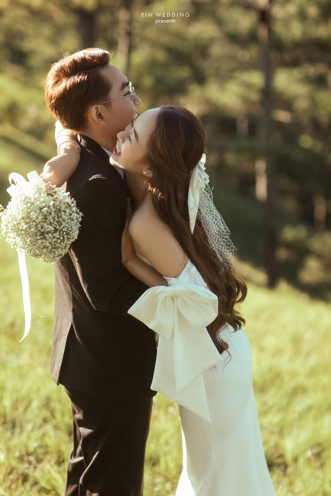 The bride kissing the groom's cheek beneath pine trees at Đồi Thông Đà Lạt