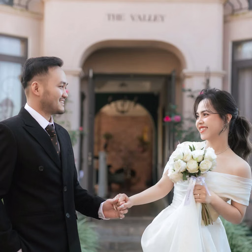 The couple hold hands and smile before the building entrance at The Nest, Đà Lạt