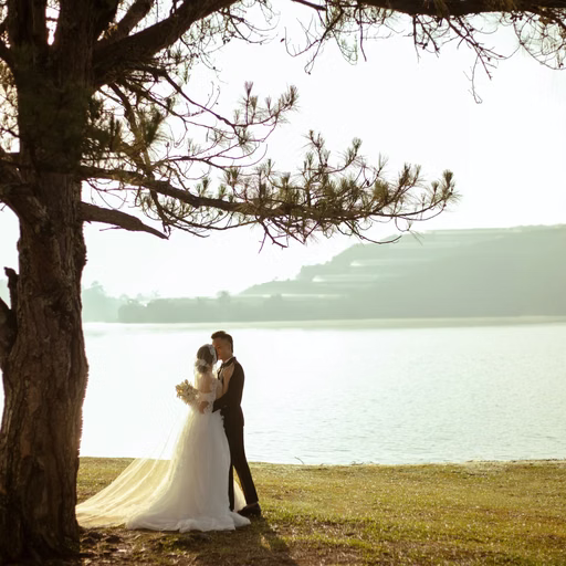 The couple embrace beneath a lakeside pine at Cây Thông Cô Đơn, Đà Lạt