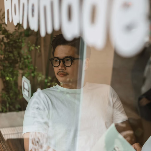 A man wearing glasses reading a newspaper behind a Đà Lạt café window.