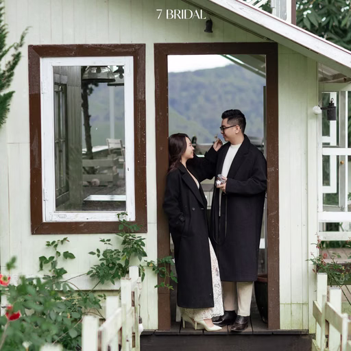 A couple beside the door of a white house in a Đà Lạt café garden.