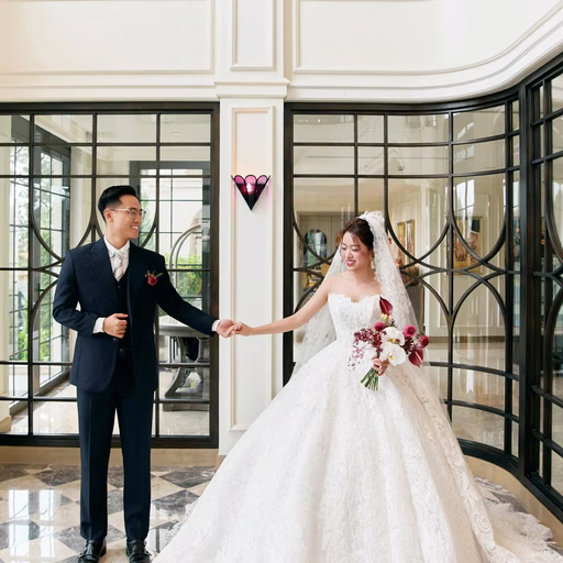 A bride and groom hold hands in a lobby with a curved staircase.