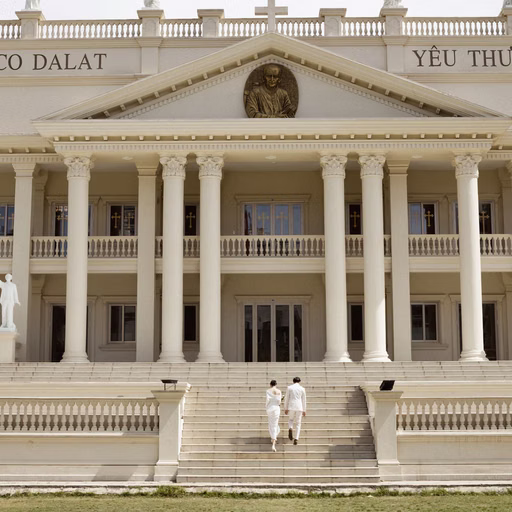 The bride and groom stand on steps beneath the colonnade at Nhà thờ Don Bosco