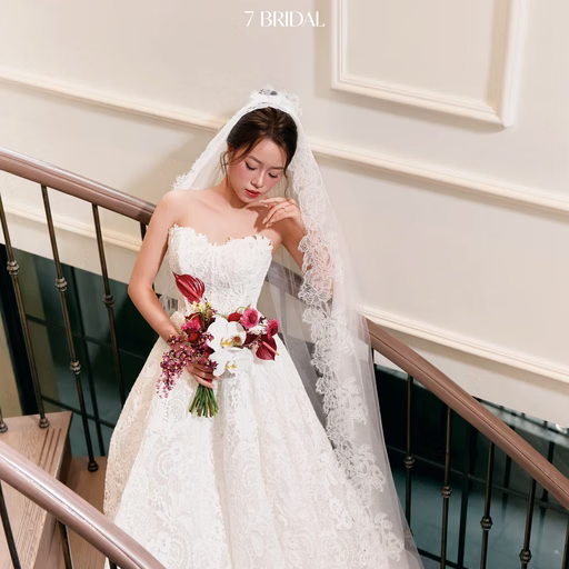 The bride holds red-and-white flowers beside a stair railing.