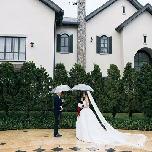 The bride and groom beneath an umbrella before a white resort villa.