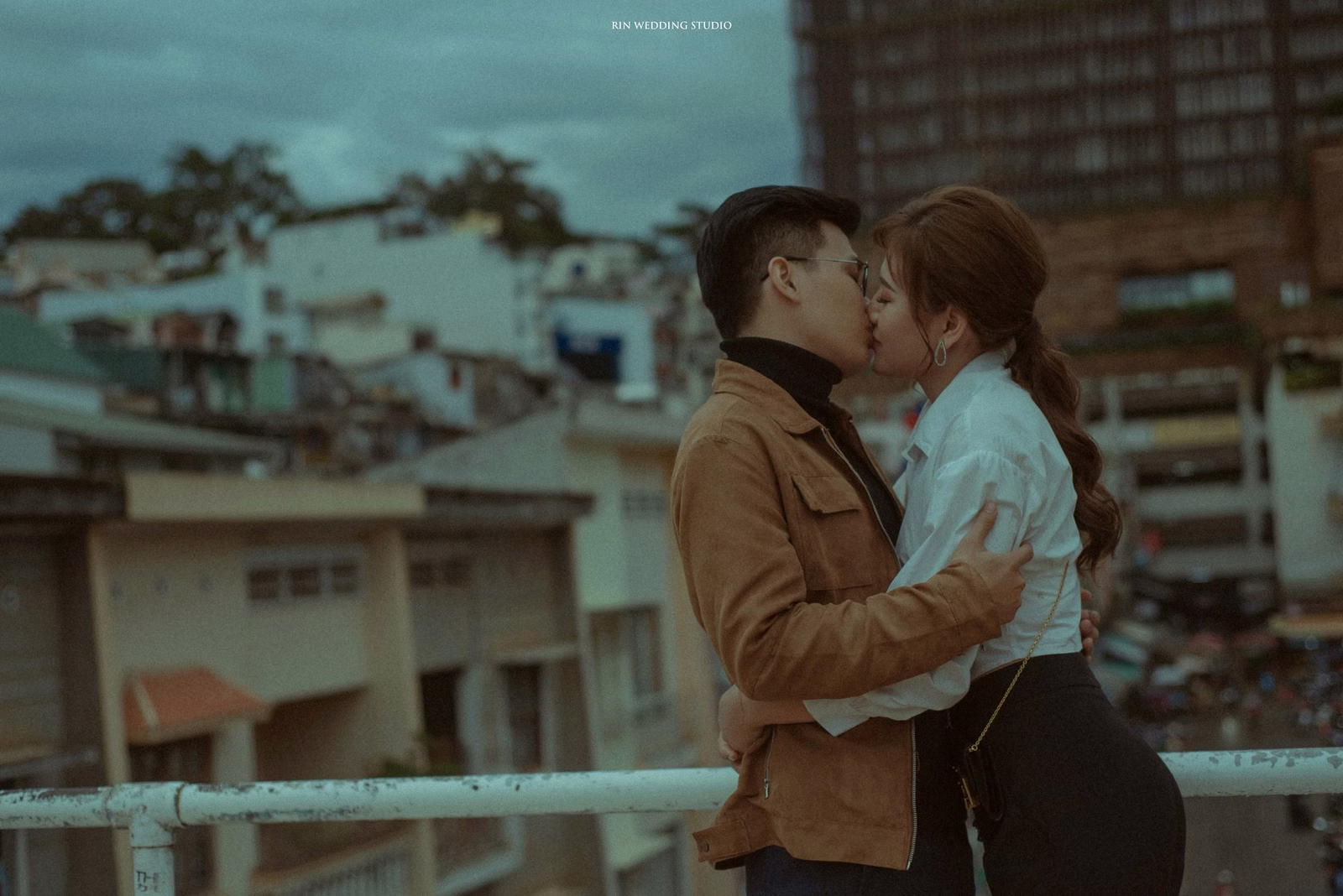 The couple embrace on a balcony overlooking Đà Lạt rooftops.