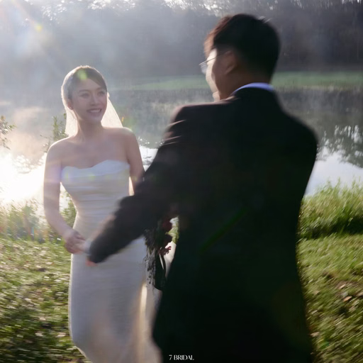 Chú rể nắm tay cô dâu trên bãi cỏ ven hồ.