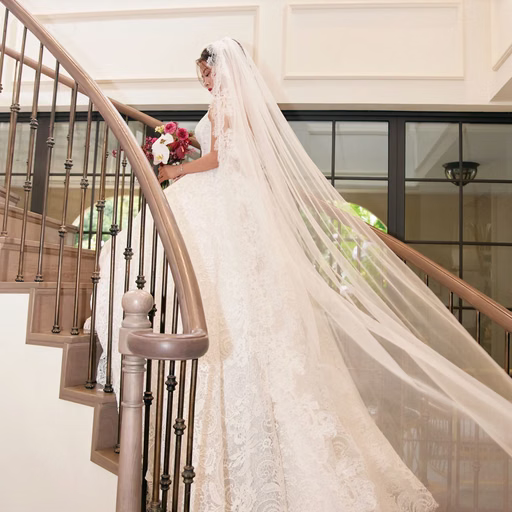 The bride with a long veil stands on a resort staircase.