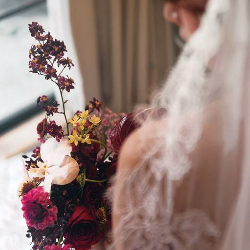 The bride admires her wedding bouquet by a window.