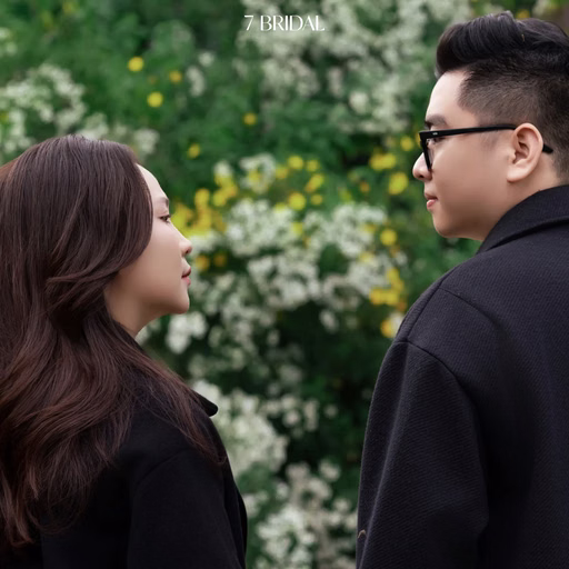 The couple look at each other before white flowers in a café garden.