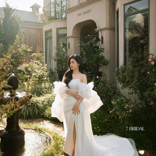 The bride in a white dress holds flowers beside a garden pond at The Nest, Đà Lạt