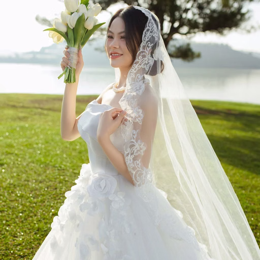 A bride holding a white bouquet on a lakeside meadow at Cây Thông Cô Đơn, Đà Lạt