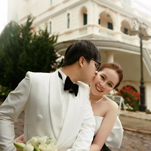 The groom kisses the bride's cheek before the hotel's historic architecture.