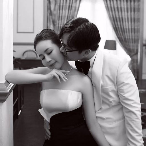 Black-and-white wedding photograph of the groom kissing the bride's shoulder indoors.