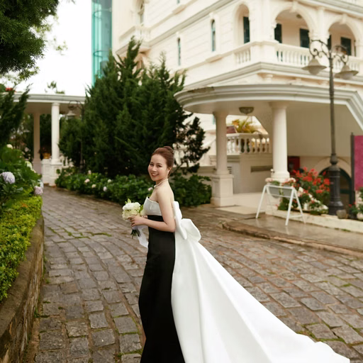 The bride holding flowers before a historic building, with a long train.