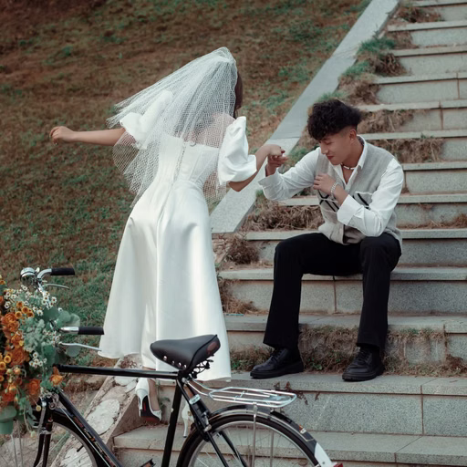 The bride holds the groom's hand while seated on steps beside a flower-decorated bicycle.