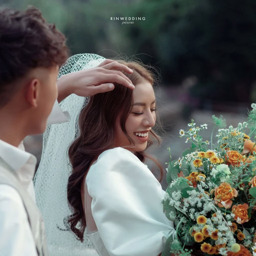 The groom adjusting the bride's veil beside an orange bouquet.