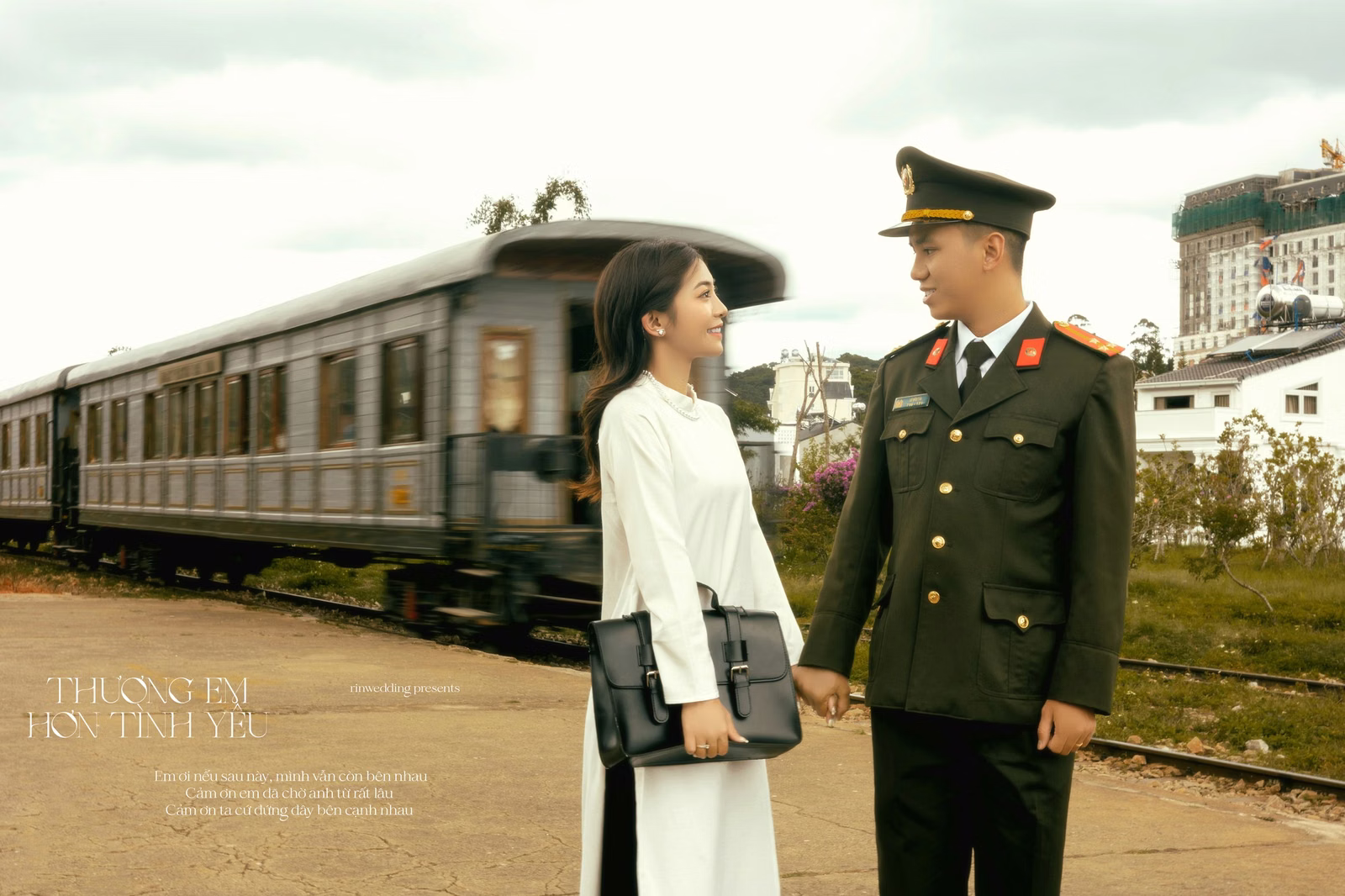 The couple holds hands before a vintage train carriage at Ga Đà Lạt.