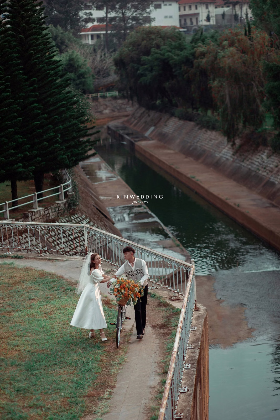 The couple walks on a lakeside path at Công Viên Ánh Sáng Đà Lạt.
