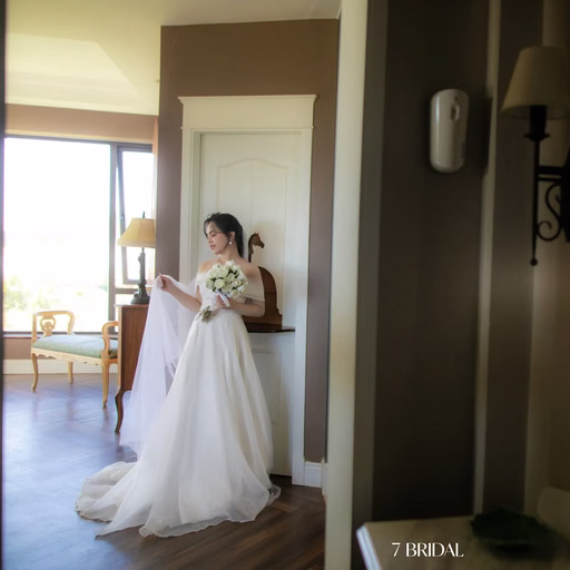 A bride holds flowers in a room, with the groom reflected in a mirror, at The Nest, Đà Lạt