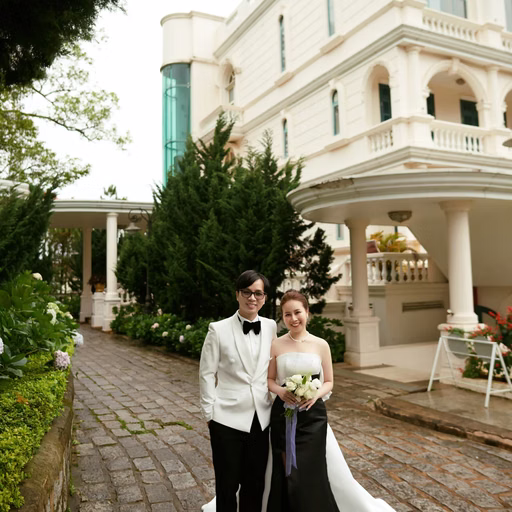 The bride and groom hold hands on a stone path before the hotel.