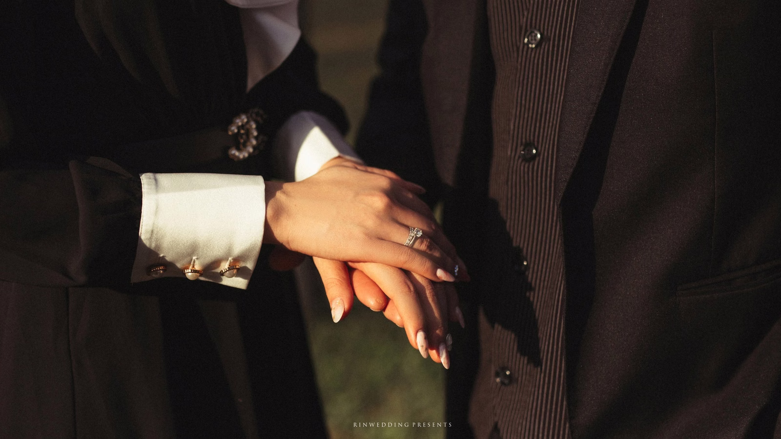 Close-up of the bride's hand resting on the suited groom's hand.