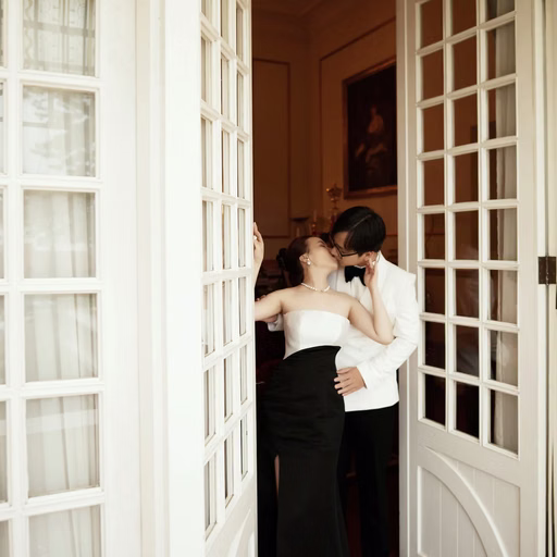 The groom embraces the bride beside wide-open white doors.
