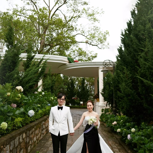 The bride and groom holding hands in a garden with a white floral trellis.