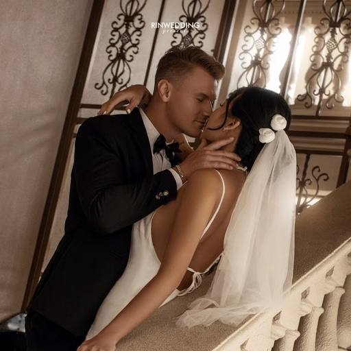 A groom kisses the bride's shoulder beside a stair railing at Don Bosco Đà Lạt.