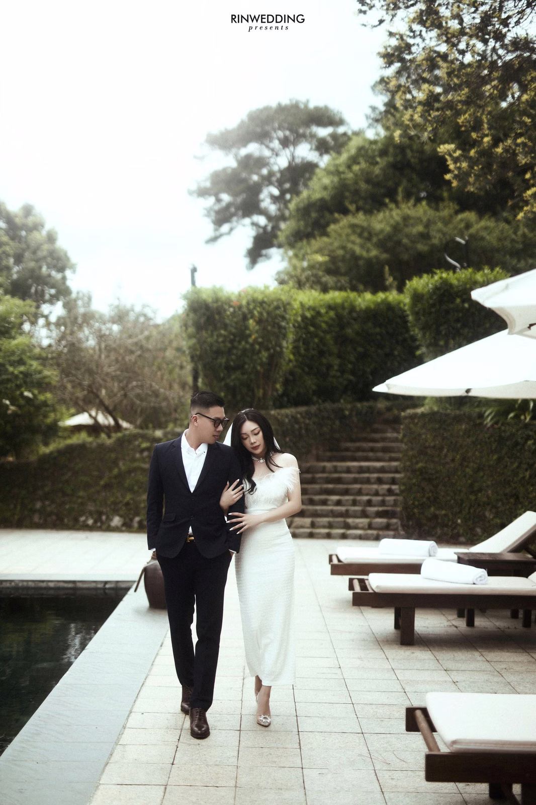 The bride and groom walk beside a resort pool.