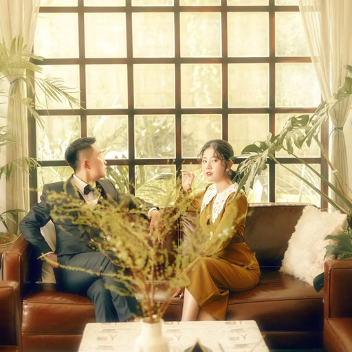 The couple chats on a sofa beside a large window in a Đà Lạt café.