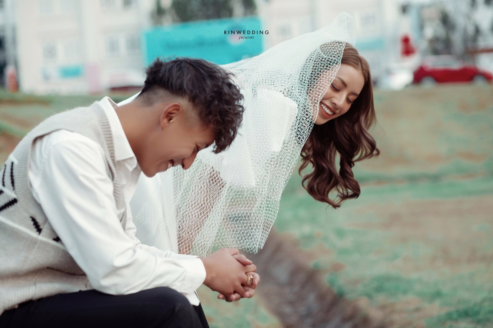 The groom bowing his head beside the bride beneath a white veil.