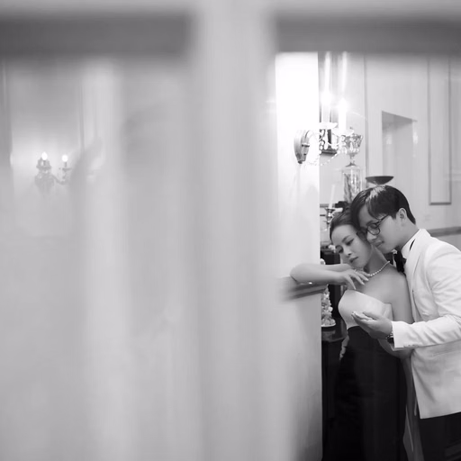 Black-and-white wedding photograph of a groom embracing and kissing the bride indoors.