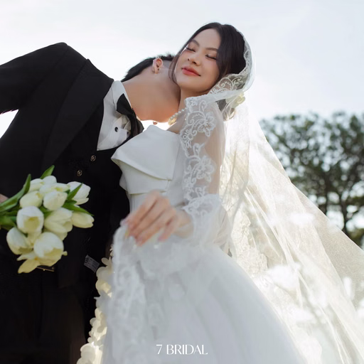 The groom bends to kiss the bride's cheek as she holds white flowers at Cây Thông Cô Đơn, Đà Lạt