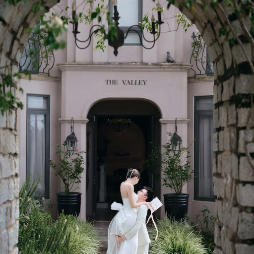 The bride reads beneath an arch of trees before the building at The Nest, Đà Lạt