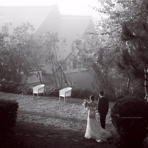 Black-and-white wedding photograph of the bride and groom before a villa with a pitched roof.