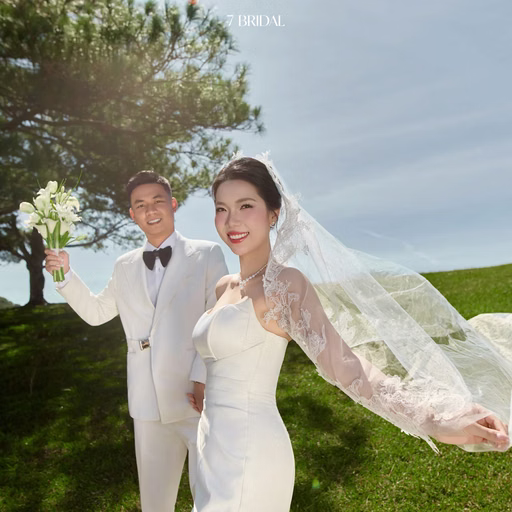 A bride spreads her veil while the groom holds flowers and smiles on the grass at Cây Thông Cô Đơn, Đà Lạt