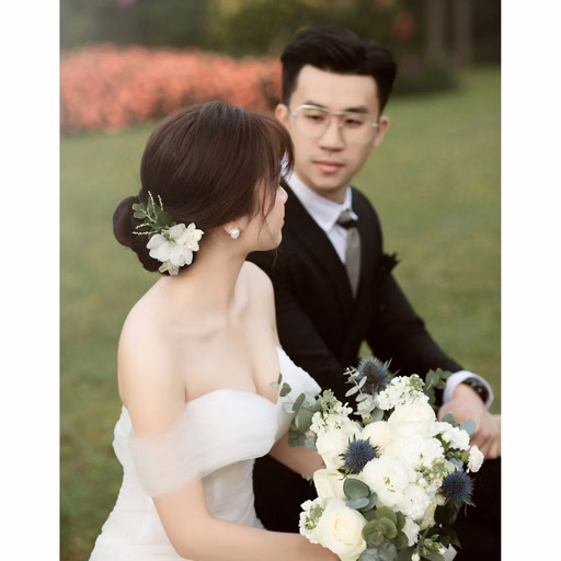 The bride holds white flowers beside the groom in a garden.