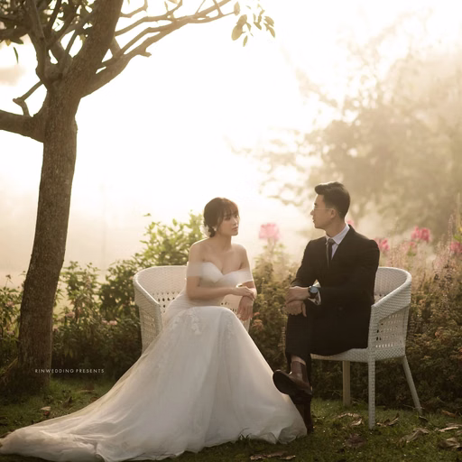 The bride and groom sit together in a sunlit garden.