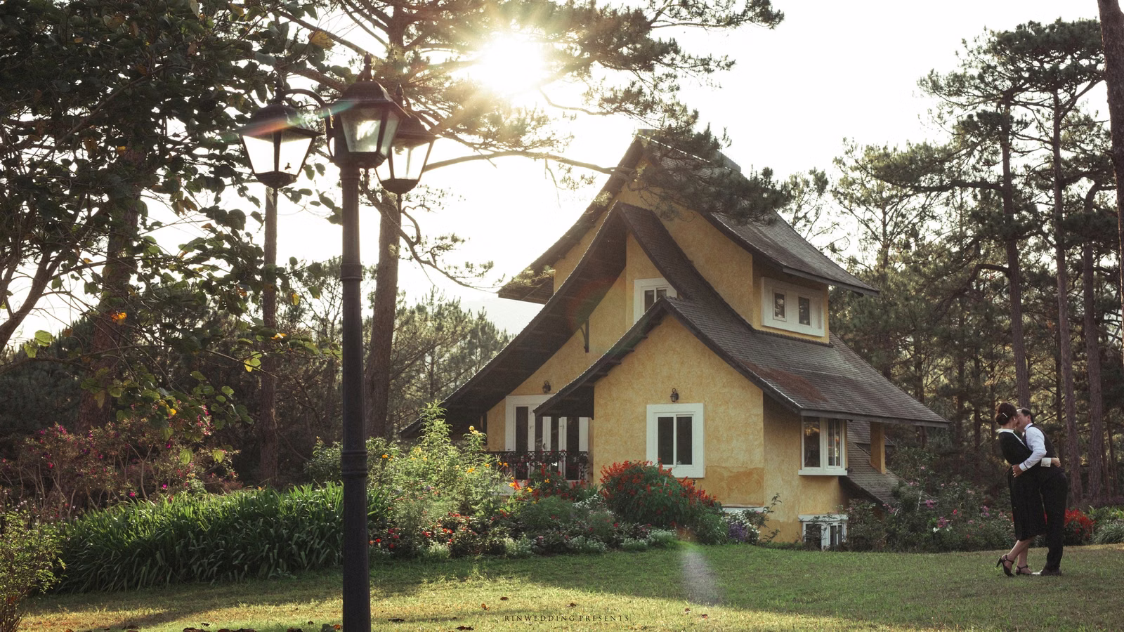 The bride and groom play on the lawn before a villa with a pitched roof.