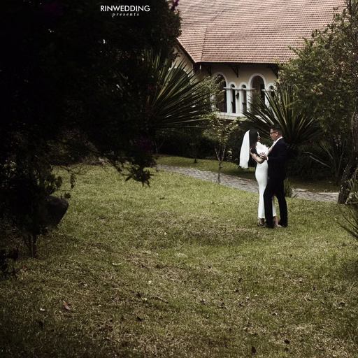 A bride and groom embrace on the lawn before a villa.
