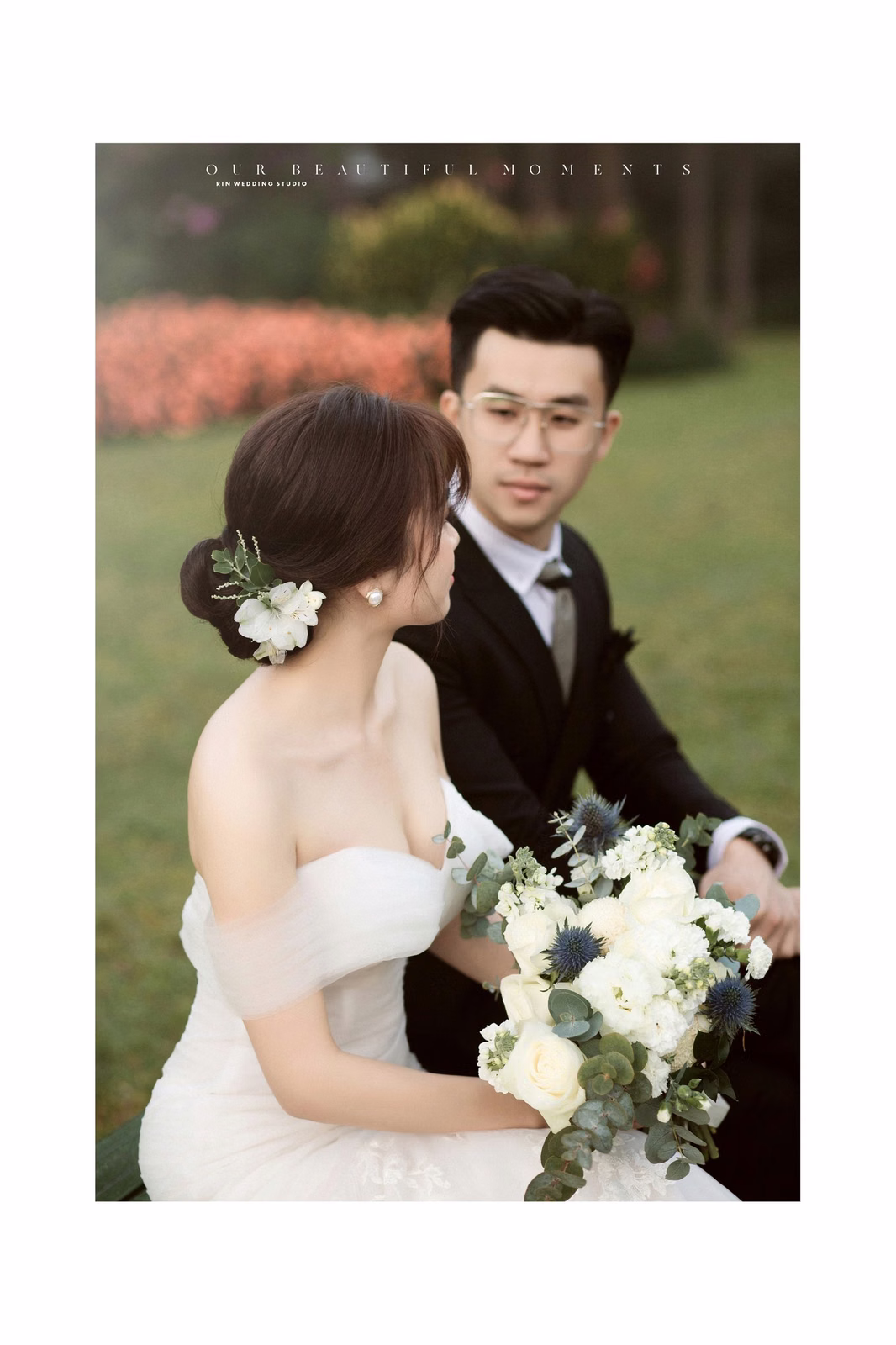 The bride holds white flowers beside the groom in a garden.