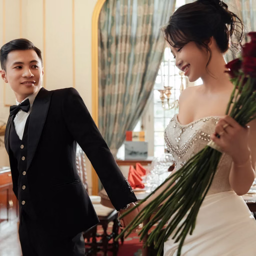 The bride holding a red bouquet beside the groom in a living room.